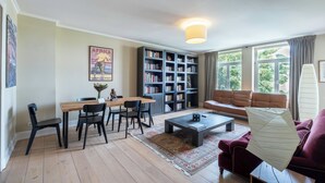 A living room with a wooden coffee table, a sofa, a bookshelf, and a dining area with chairs and a table. - Brussels EU Prestige residence (Brussels)