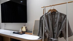 Une salle de bain moderne avec un plan de toilette blanc, un miroir, un peignoir suspendu à un porte-peignoir et un rideau noir.