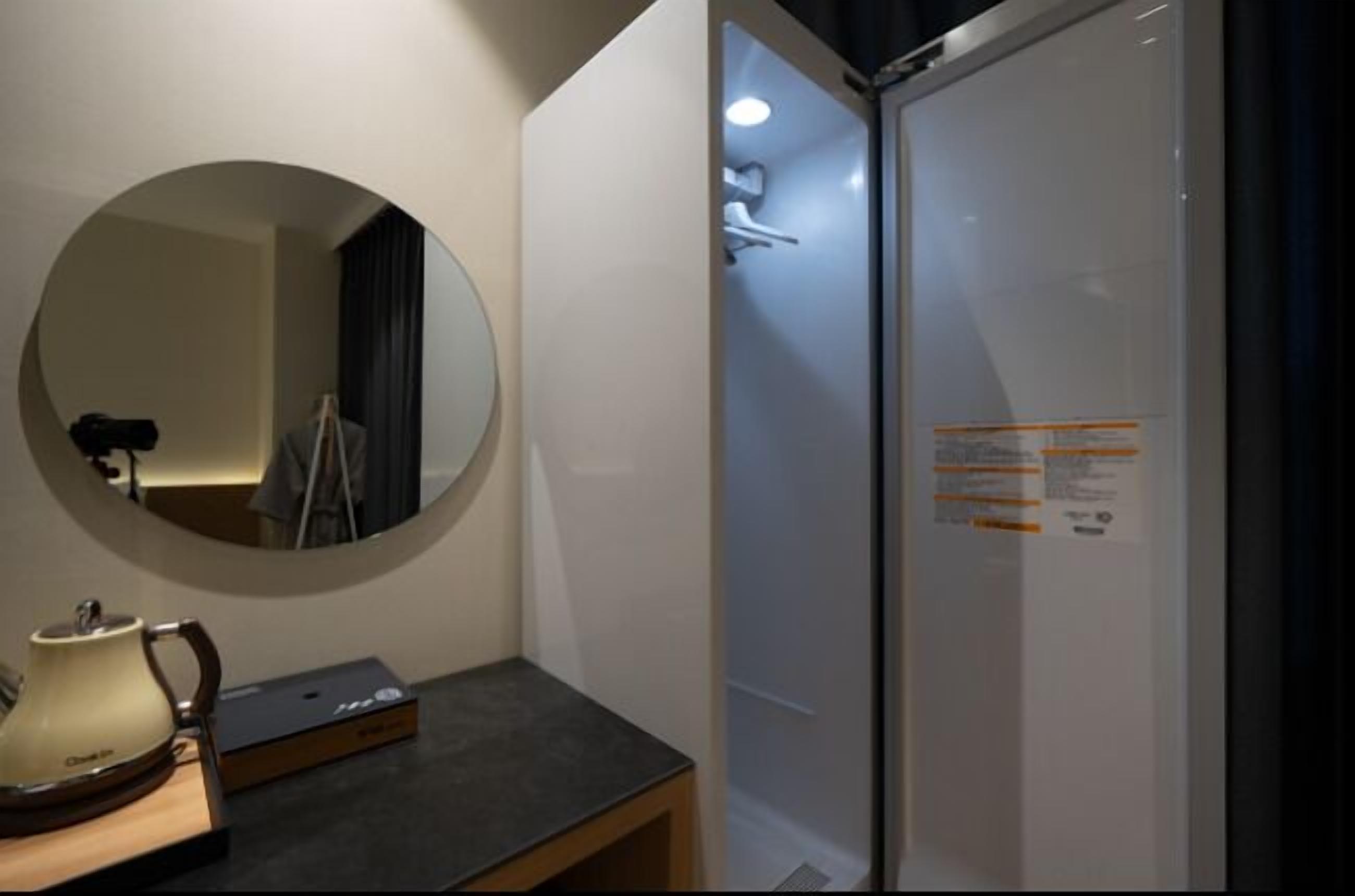 A modern bathroom with a round mirror, a small table with a teapot, and a glass shower enclosure.