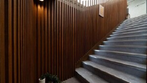 Un escalier dont les murs sont recouverts de lambris en bois, et un vase blanc orné de verdure, placé à sa base.