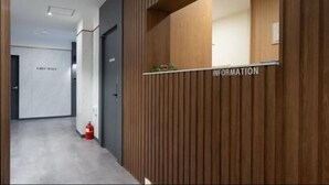 Un espace d’accueil avec un mur recouvert de panneaux en bois, un comptoir de réception et un extincteur posé sur le sol.