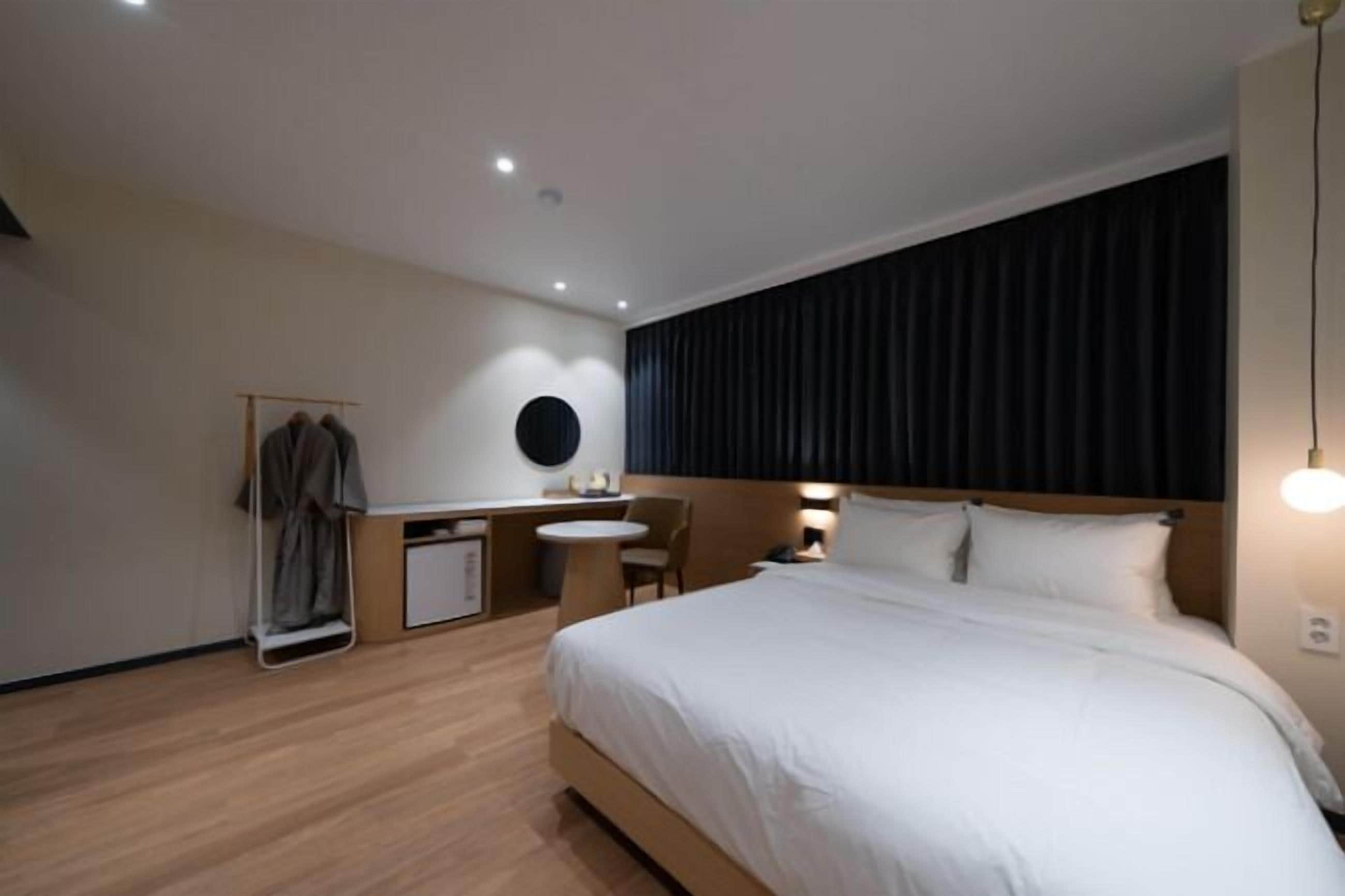 A hotel room with a bed, a desk, a chair, a small table, and a wardrobe.