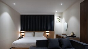 Une chambre d’hôtel moderne avec un grand lit, des tables de chevet, un canapé, un miroir et une petite table avec une bouilloire.
