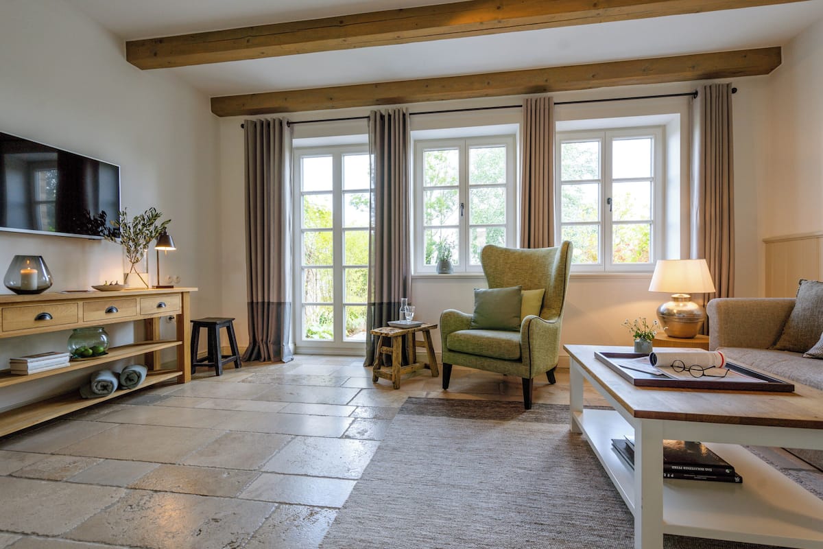 A living room with a wooden ceiling, a green armchair, a sofa, a coffee table, a TV, and a bookshelf.