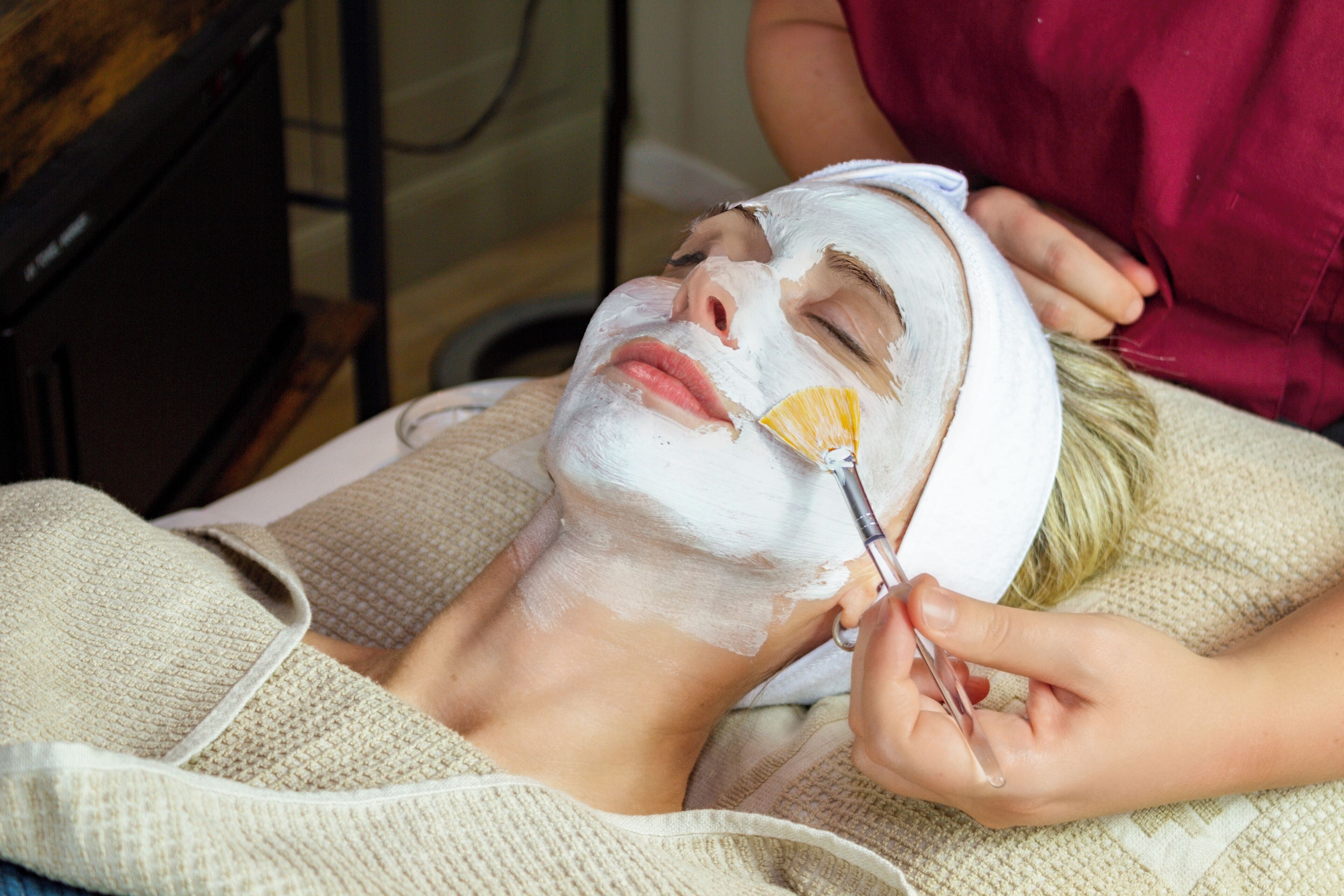 A person lying down with a facial mask applied, being attended to by another person.