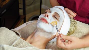A person lying down with a facial mask applied, being attended to by another person.