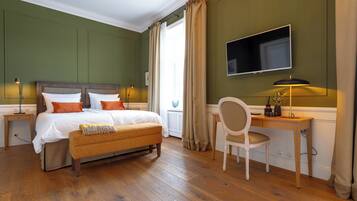 A bedroom with a wooden bed, a desk, a chair, a TV, and a window with curtains.