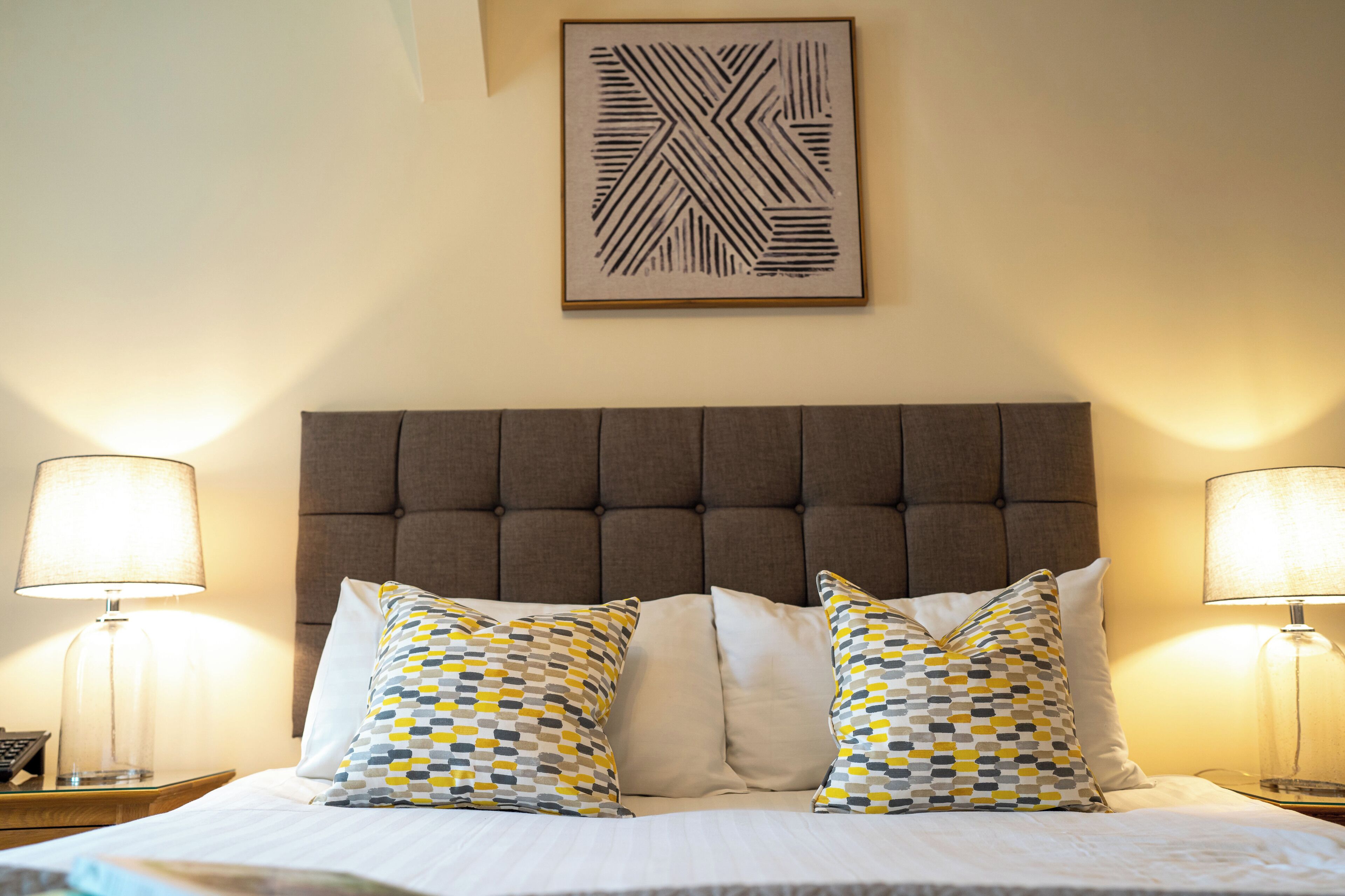 A neatly made bed with patterned pillows, a tufted headboard, and two bedside lamps.
