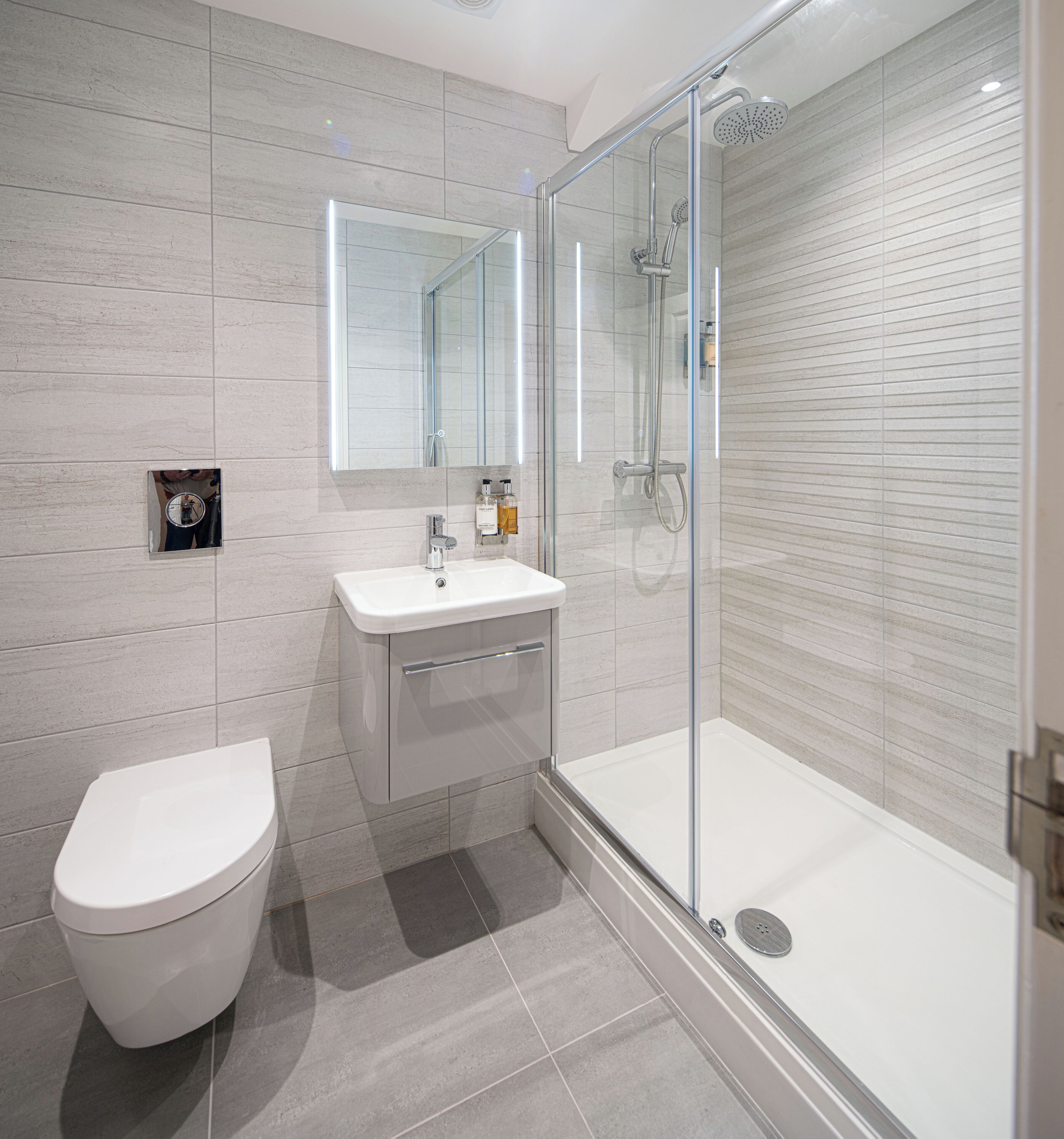 Un baño moderno con inodoro, lavamanos y ducha con mampara de vidrio.