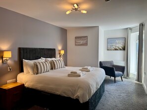 A hotel room with a large bed, two bedside lamps, a chair, and artwork on the walls.