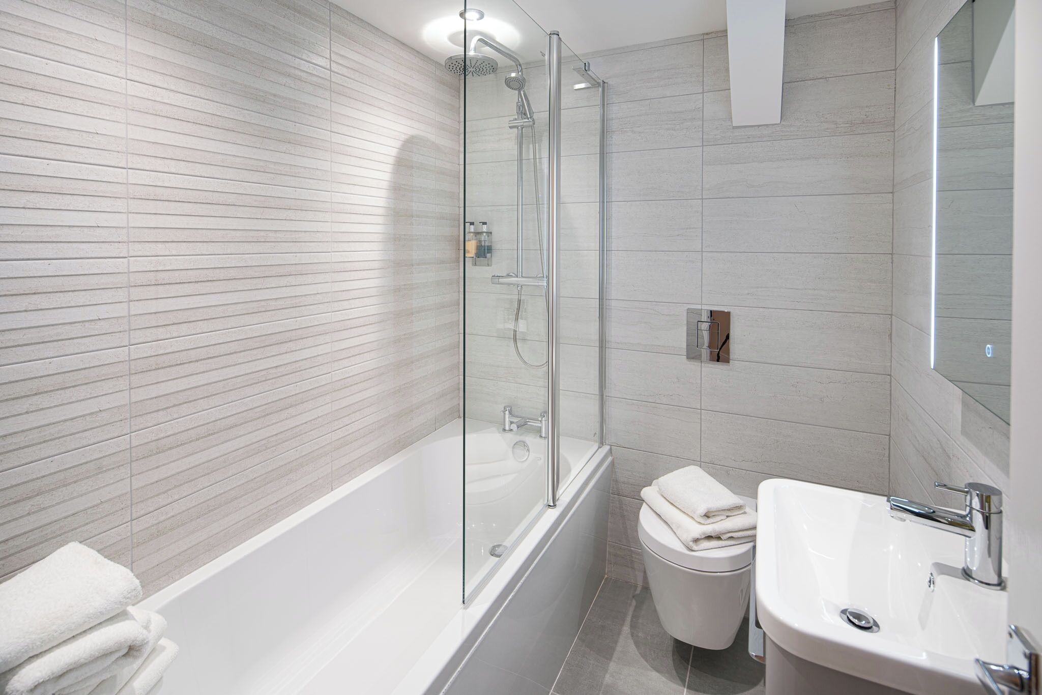 A modern bathroom with a glass-enclosed shower, a white bathtub, and a sink.