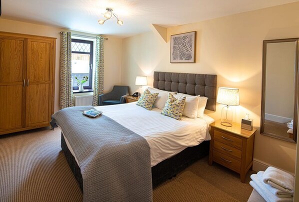 A neatly arranged bedroom with a large bed, bedside tables, a wardrobe, and a window with curtains.