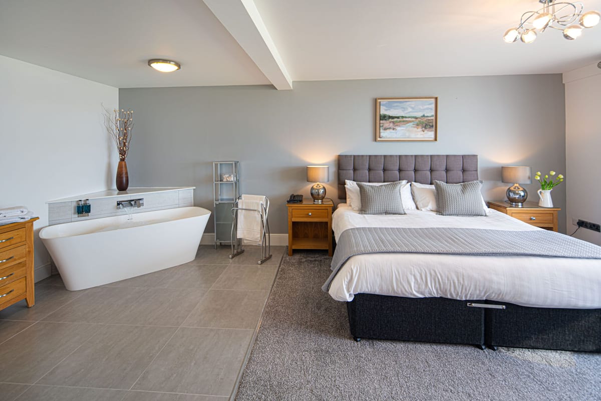 Ein modernes Schlafzimmer mit einem großen Bett, einer separaten Badewanne und einem Nachttisch mit einer Lampe.