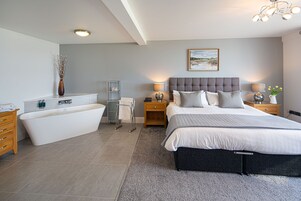 Un dormitorio moderno con una cama grande, una bañera independiente y una mesita de noche con lámpara.