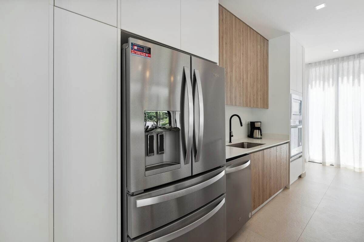 A modern kitchen with a stainless steel refrigerator, wooden cabinets, a built-in oven, and a sink.