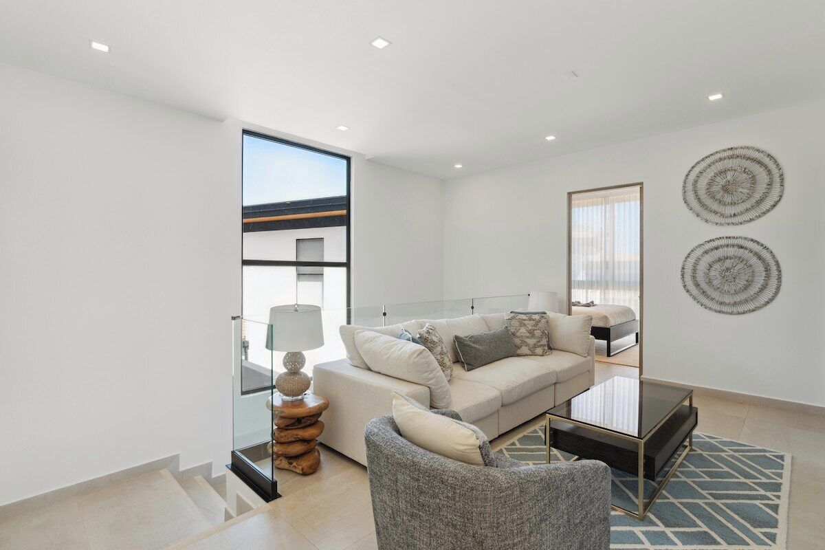 A modern living room with a sofa, armchair, and coffee table. There is a staircase leading to an upper level.