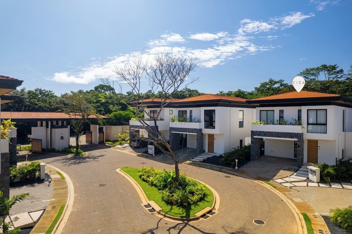 A modern residential area with a central road, surrounded by houses with white exteriors and red roofs.