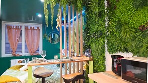 Une pièce avec un mur vert, une fenêtre avec des rideaux, une table en bois sur laquelle se trouvent une bouteille, des verres et un menu.