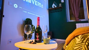 Une pièce avec un écran de projection affichant le titre d’un film, une bouteille de vin, deux verres et une petite table.