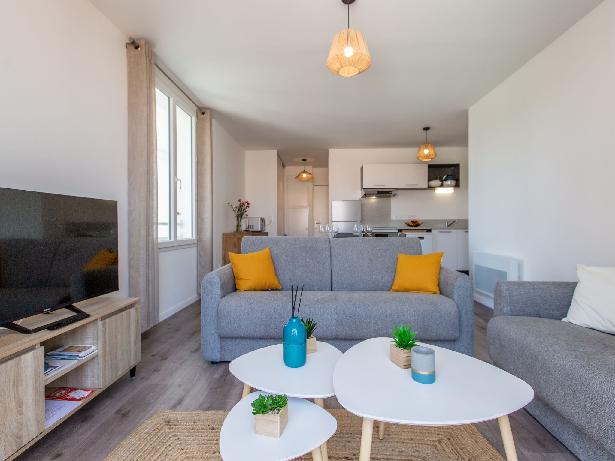 Ein modernes Wohnzimmer mit einem grauen Sofa, zwei weißen Couchtischen und einem Fernseher auf einem Holzboden.