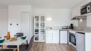 Moderni keittiö, jossa on valkoiset kaapit, sisäänrakennettu mikroaaltouuni, kahvinkeitin ja astianpesukone.