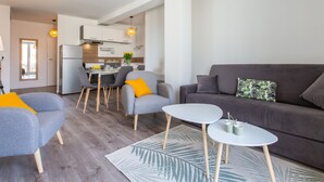 A modern living room with a grey sofa, two armchairs, and a small white table. A kitchen is visible in the background with a dining area. - Cap Océan by Interhome (Capbreton)