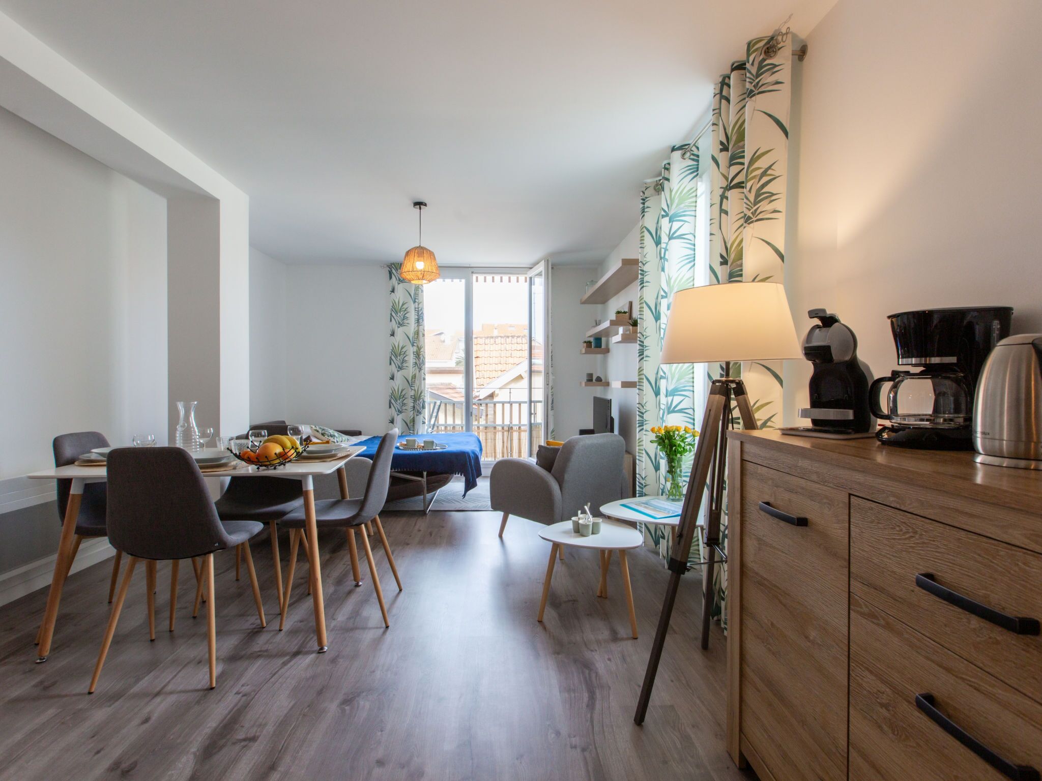 A modern dining area with a table set for two, a coffee maker, and a lamp on a wooden cabinet.