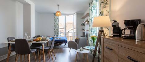 A modern dining area with a table set for two, a coffee maker, and a lamp on a wooden cabinet.