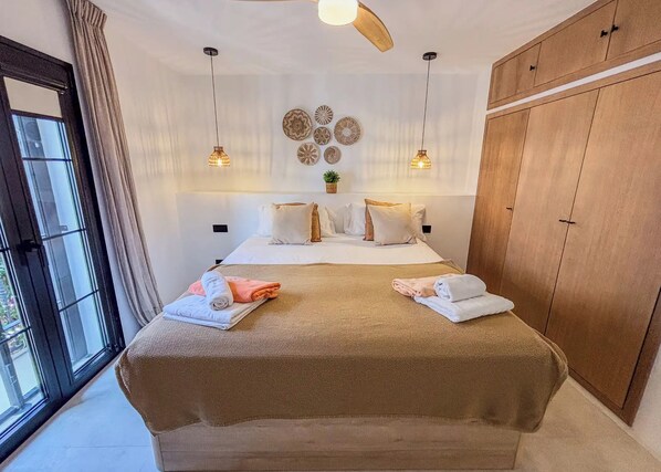 A bedroom with a bed, bedside lamps, a ceiling fan, and a large wardrobe.