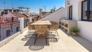 A rooftop terrace with a wooden table and wicker chairs, a potted plant, and a view of the cityscape. - Casa Gina Old Town Marbella Center 4 Bedrooms (Marbella)