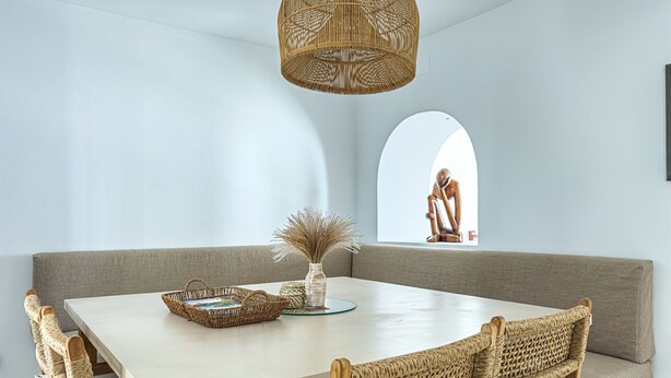 A dining area with a white table, wicker chairs, a woven light fixture, and a view of a statue through an arched window. - Casa Gina Old Town Marbella Center 4 Bedrooms (Marbella)