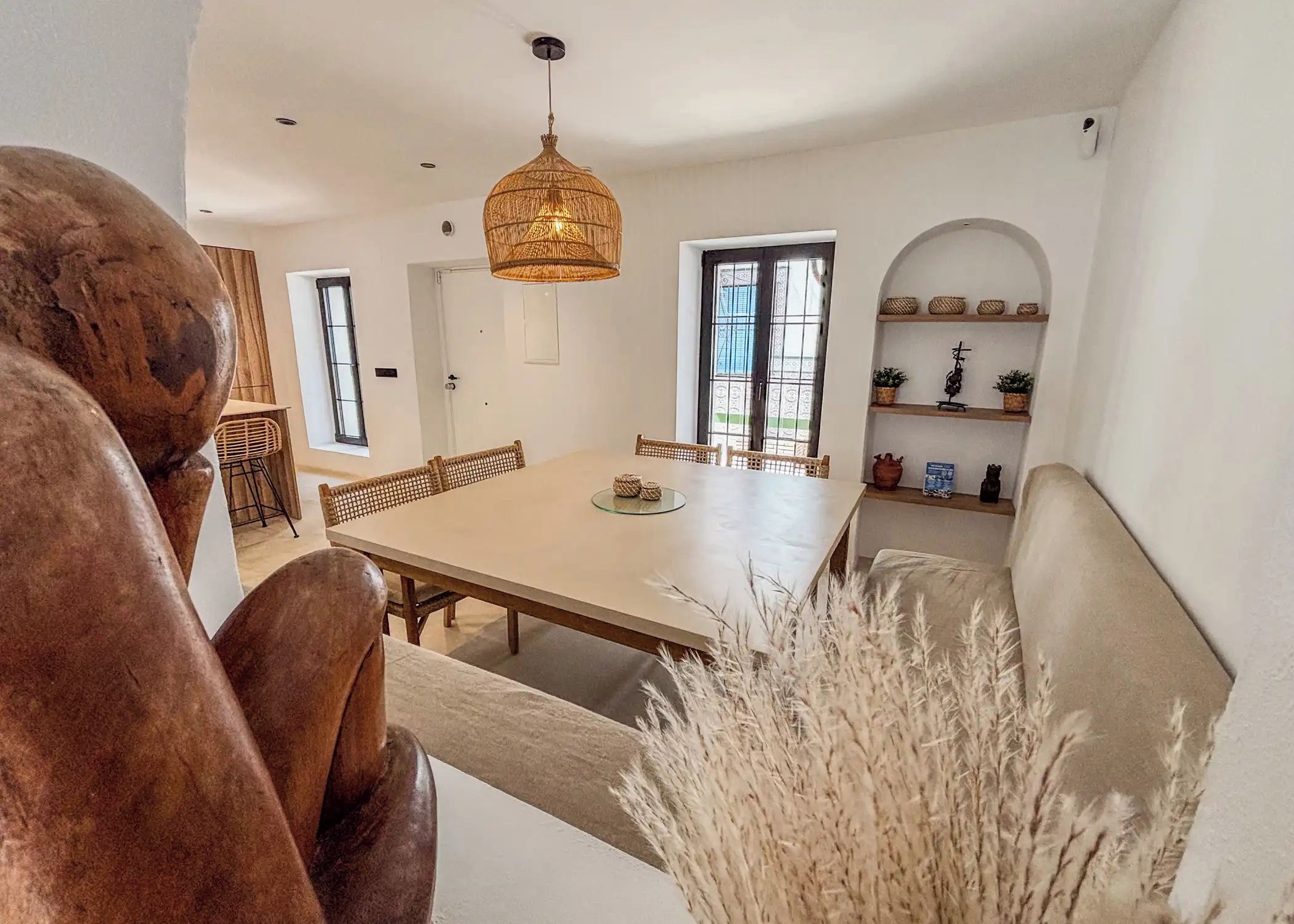 A dining area with a large table, wicker chairs, and a hanging light fixture.
