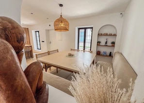 A dining area with a large table, wicker chairs, and a hanging light fixture.