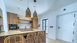 A modern kitchen with a central island, wooden bar stools, pendant lighting, and built-in appliances. - Casa Gina Old Town Marbella Center 4 Bedrooms (Marbella)