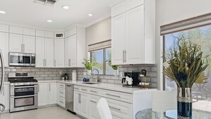 A modern kitchen with white cabinetry, stainless steel appliances, a glass table, and a view of the outdoors. - 3 King Rooms, Sleeps 12 Heated Pool, Waterslide Paradise! 30 Night Min. (Queen Creek)
