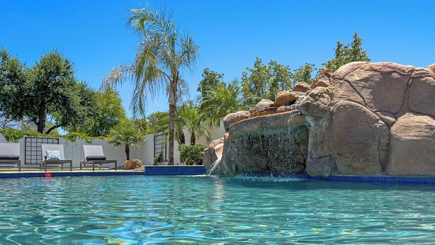 A clear pool with a rock formation and palm trees. - 3 King Rooms, Sleeps 12 Heated Pool, Waterslide Paradise! 30 Night Min. (Queen Creek)