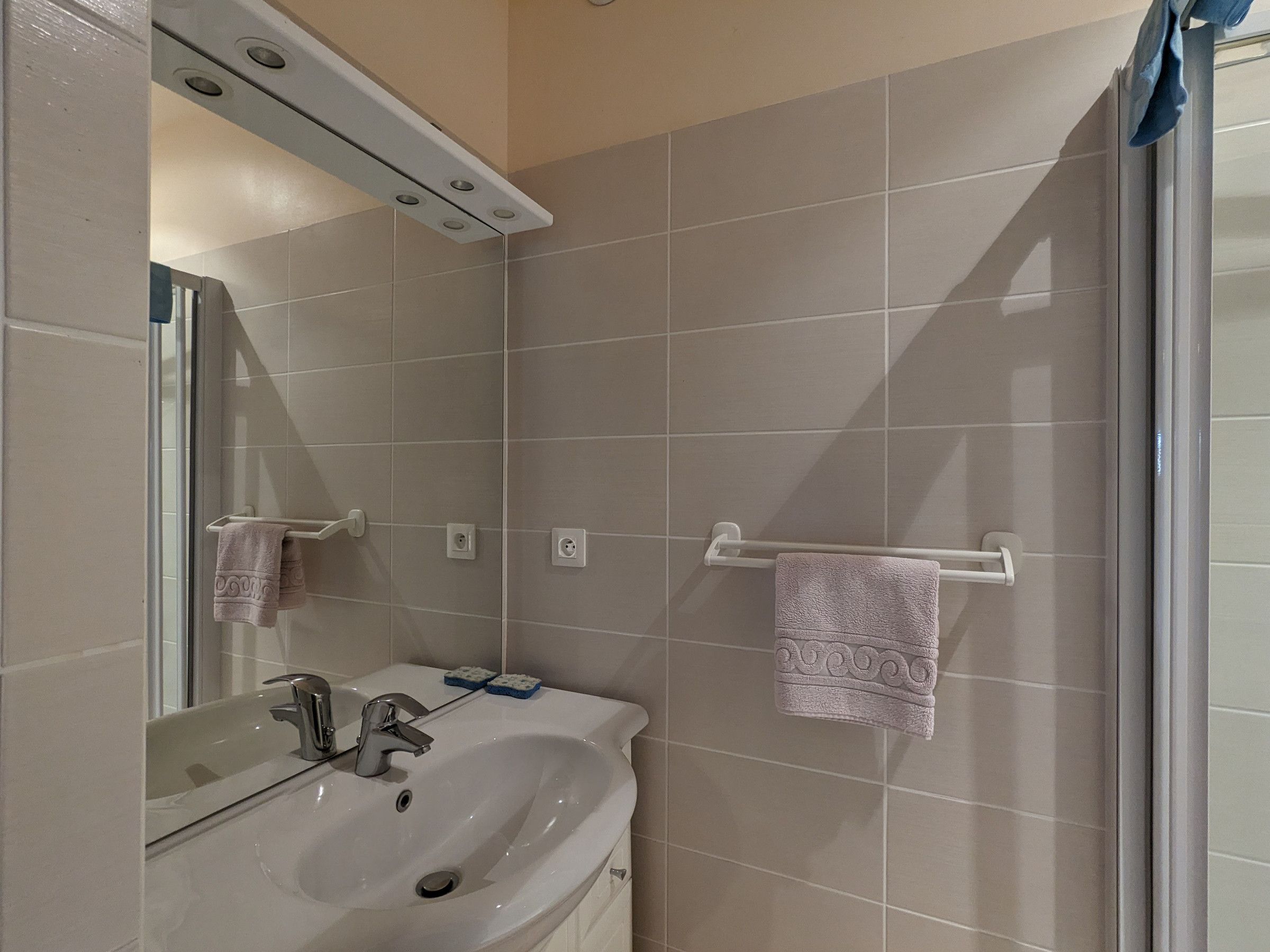 A bathroom with a sink, mirror, towel rack, and shower area.