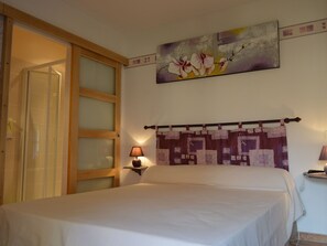 A bedroom with a bed, a nightstand, a wall-mounted lamp, a door with frosted glass panels, and a painting above the bed. - Countryside Retreat with Spacious Grounds, Pool Access, and Family-Friendly Amenities (Pérassay)