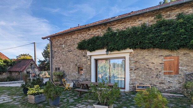 A stone house with a tiled roof, a wooden door, and a small window. There are outdoor seating and potted plants. - Countryside Retreat with Spacious Grounds, Pool Access, and Family-Friendly Amenities (Pérassay)