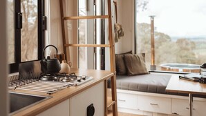 Une cuisine compacte dotée d’un plan de travail en bois, d’une bouilloire et d’un support pour la bouilloire. Une fenêtre offre une vue sur l’extérieur.