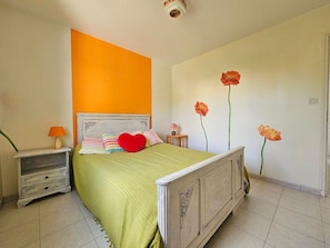 Un dormitorio con cama, mesita de noche, lámpara y un muro decorado con motivos florales.