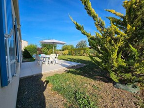 A patio area with outdoor furniture and a table, surrounded by a well-maintained lawn and trees. - Quiet Vendée House, 5 Guests, between Sea and Countryside (Saint-Michel-en-l'Herm)