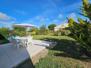 An outdoor patio with a table and chairs, surrounded by greenery and a house in the background. - Quiet Vendée House, 5 Guests, between Sea and Countryside (Saint-Michel-en-l'Herm)