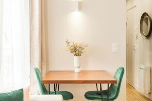 A dining area with a wooden table, two green chairs, and a white vase with flowers.