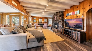 A cozy living room with a stone fireplace, a large TV, and a sofa with cushions. - Reflections Lakeview By Tahoe Getaways - Hot Tub & Buoy, Dog OK (Carnelian Bay)