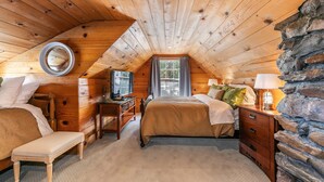 A cozy attic bedroom with a wooden ceiling, a stone wall, a bed with a wooden headboard, a desk, and a bench. - Reflections Lakeview By Tahoe Getaways - Hot Tub & Buoy, Dog OK (Carnelian Bay)