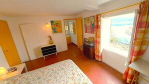 A bedroom with a bed, a dresser, a suitcase, and a window with a view. - "les Terrasses" : Maison Dans le Village, 4 Terrasses (Sainte-Croix-du-Verdon)