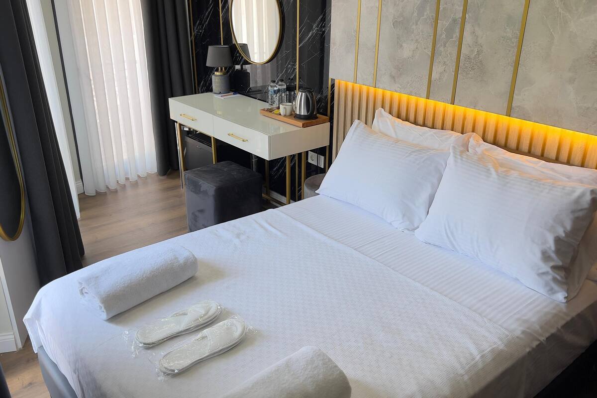 A hotel room with a bed, a desk, a chair, and a mirror.