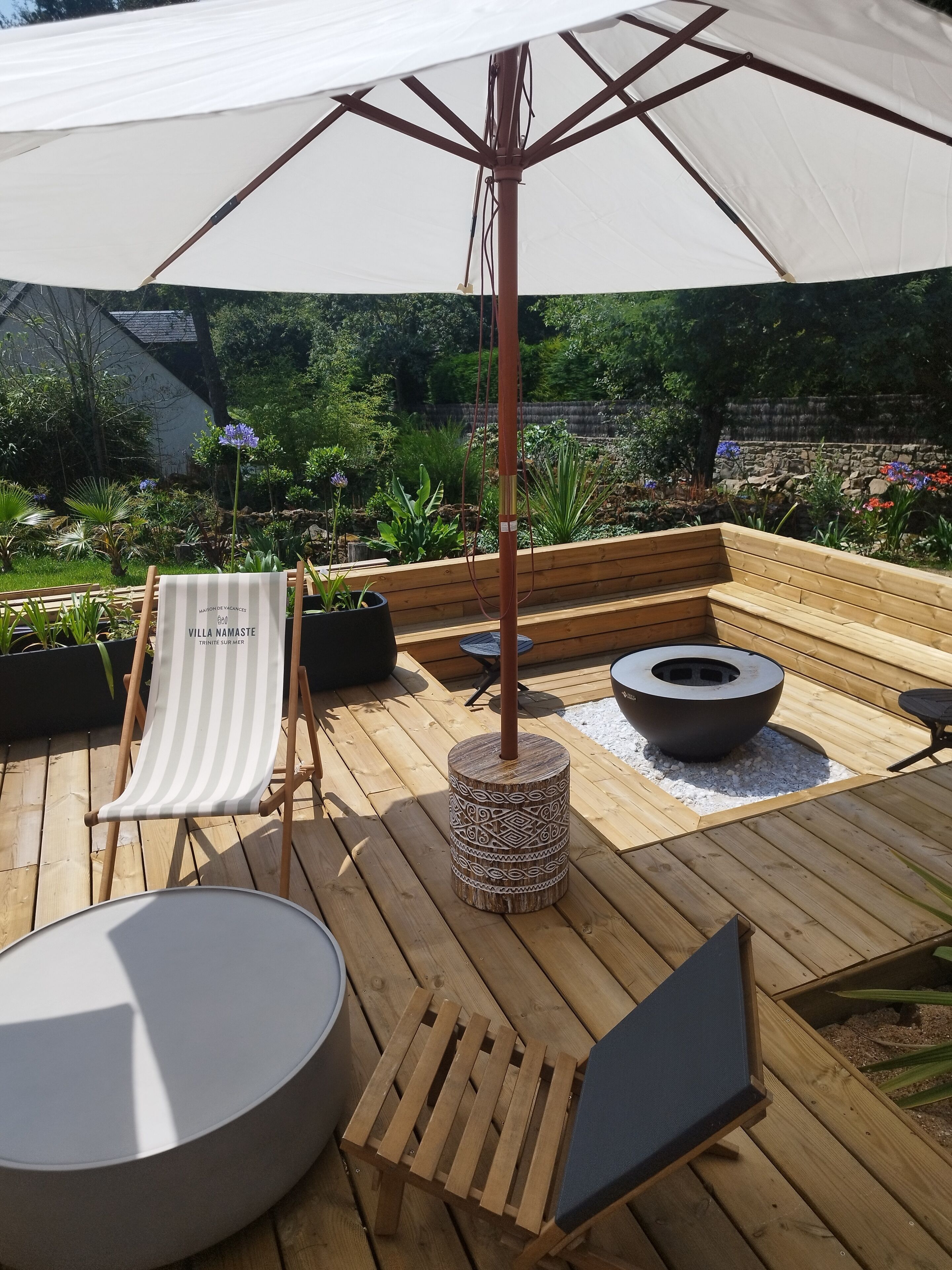 A wooden deck with a lounge chair, a round table, and a fire pit.
