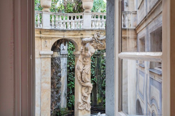 A view through a window of a building with a stone balustrade, a decorative archway, and a statue. - Garibaldi Glamorous Apartment by Wonderful Italy (Genoa)
